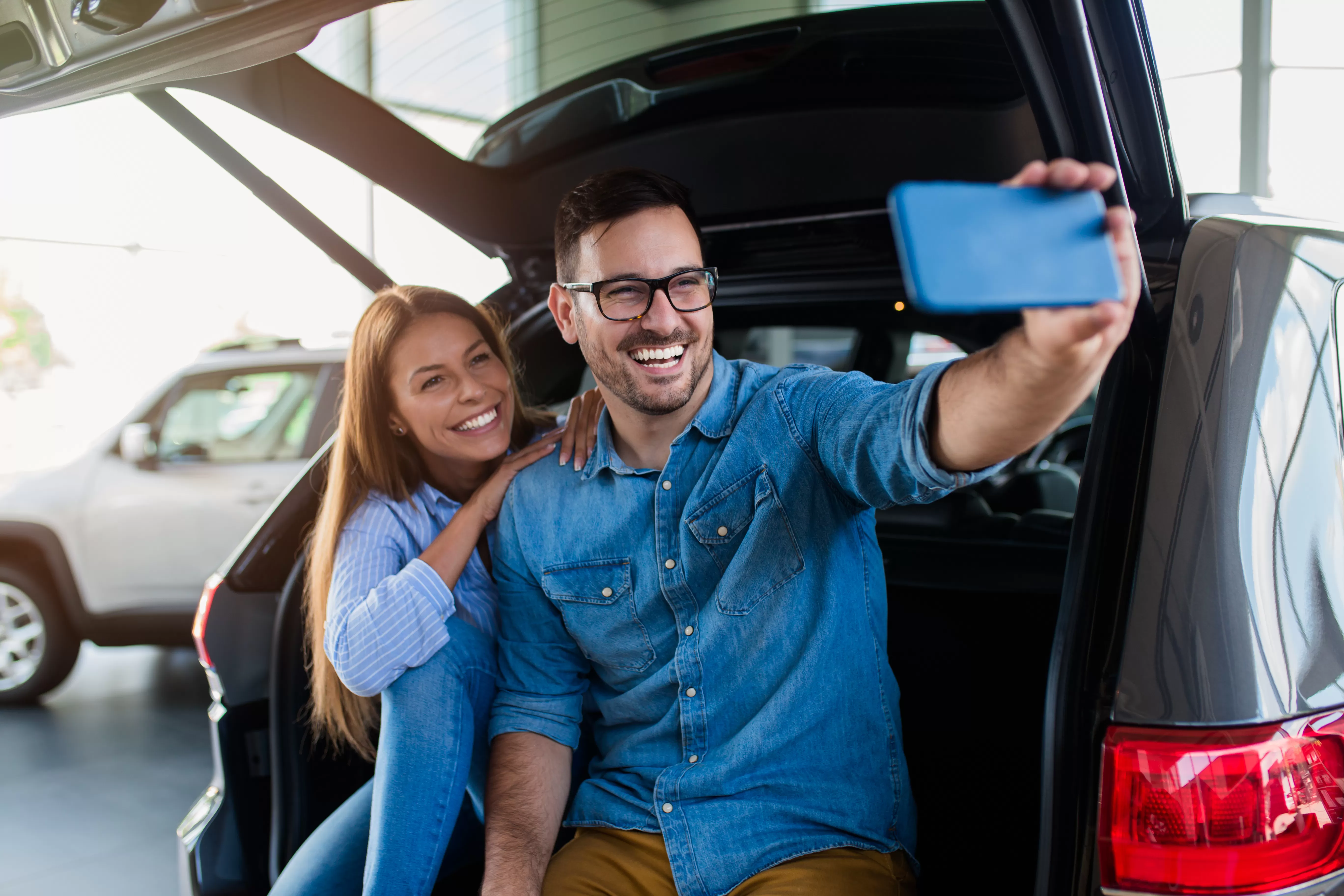 A young couple takes a selfie while checking out new cars after learning about auto loan terms.