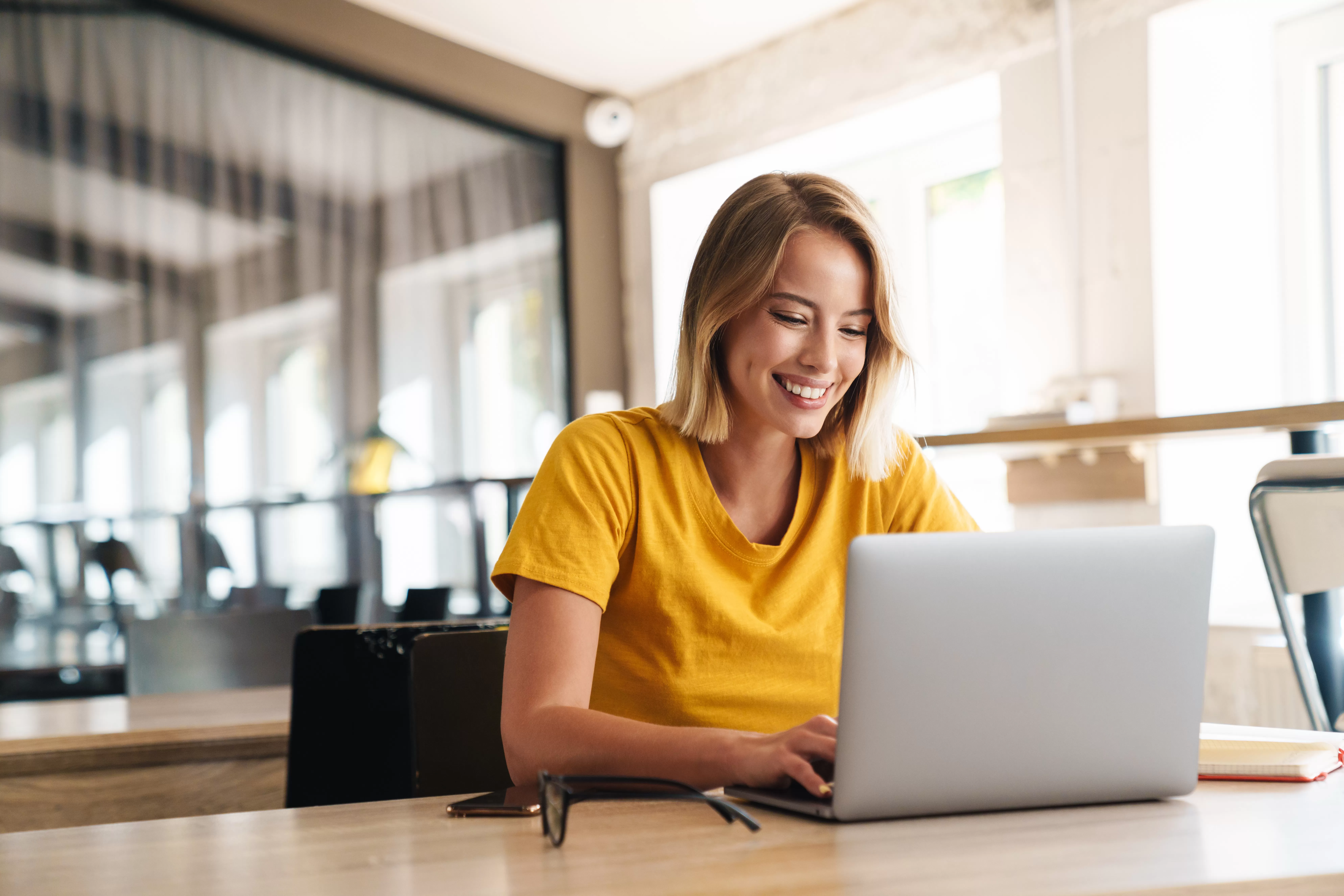 Woman in a bright yellow shirt smiling at her laptop