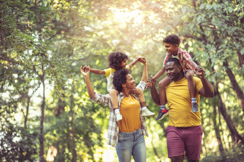 amily walking through park with children on parents shoulders