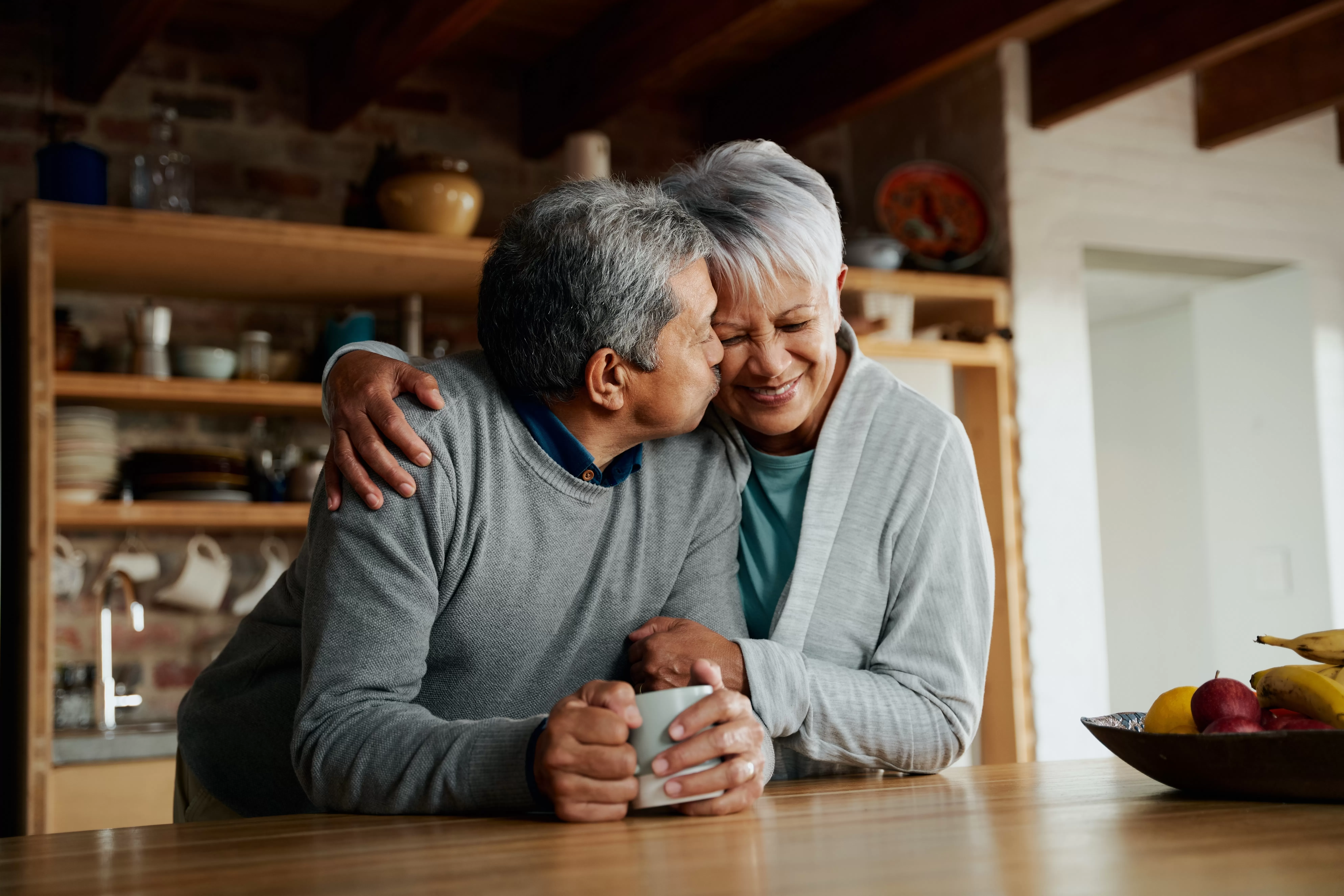 A senior couple embraces in their kitchen.